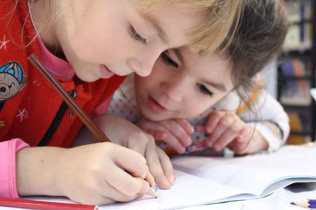 Two young children learning to write together, focused on a notebook.