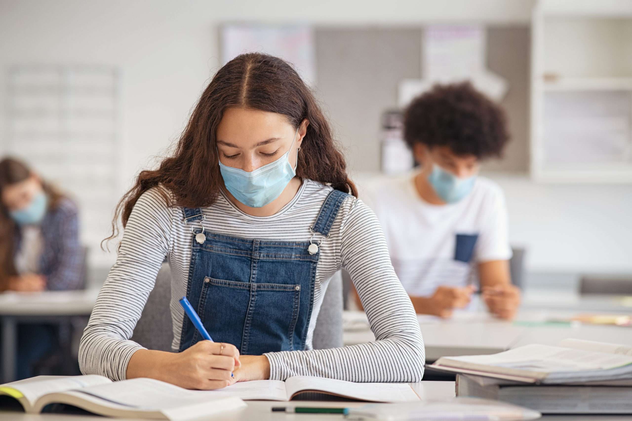 High school student taking notes from book while wearing face mask