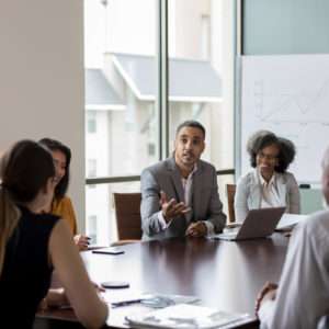 Mid adult businessman gestures as he discusses sales with a group of colleagues during a meeting.