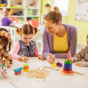 Happy female teacher teaching small kids how to draw at preschool.