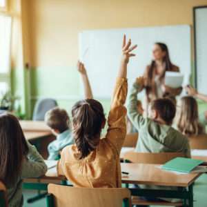 Students raising hands while teacher asking them questions in classroom