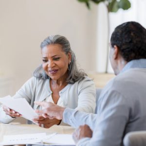 Senior woman smiles as unrecognizable male insurance agent explains paperwork