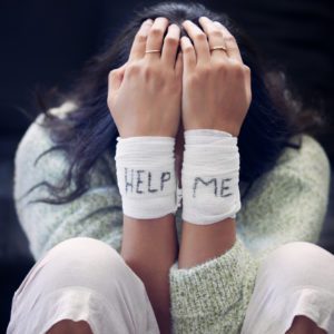 Shot of a young woman with bandages wrapped around her wrists showing “help” written on them